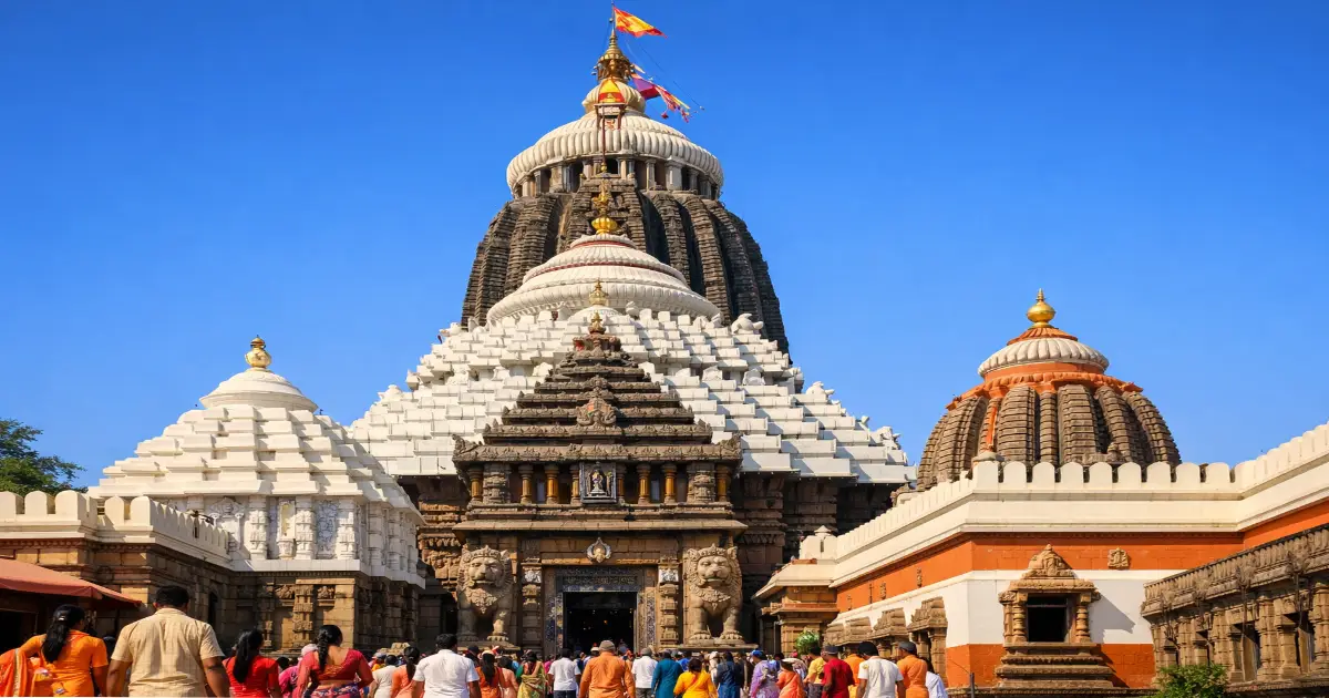 Low-angle view of Shree Jagannath Temple in Puri with its towering vimana, golden kalasha, and devotees gathered below under a clear blue sky.